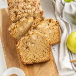 Several slices of apple bread on a wooden board, a kitchen cloth, white surface.