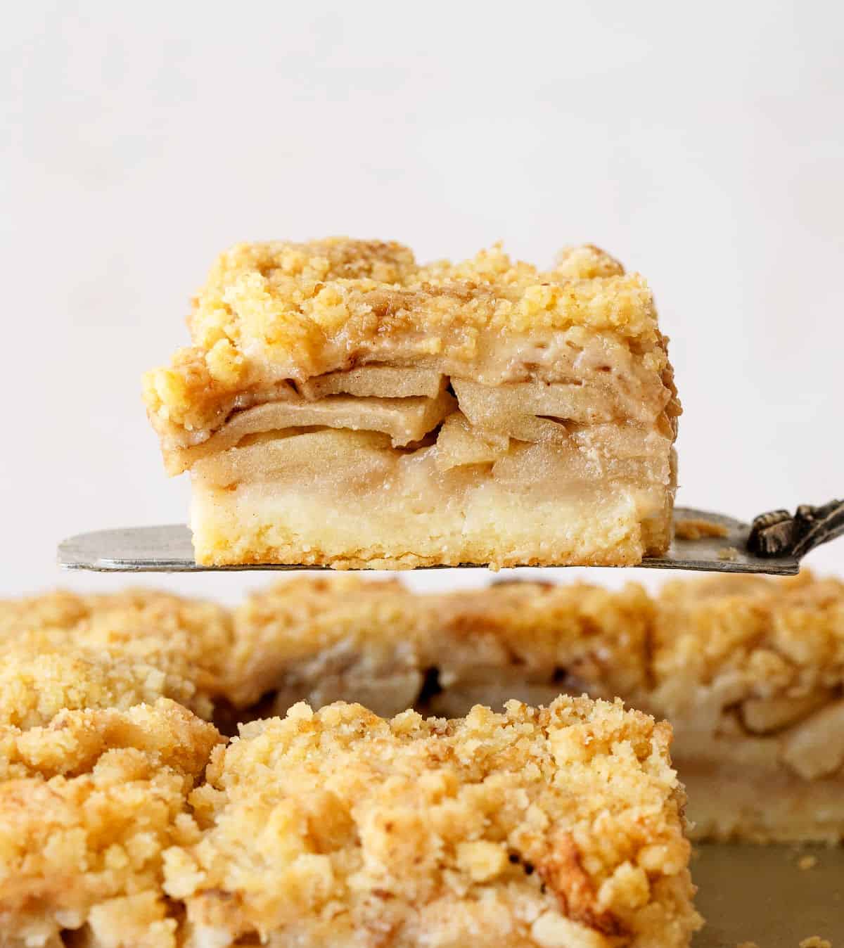 Single serving of apple pie crumb bars on a metal cake server with rest of bars below. 