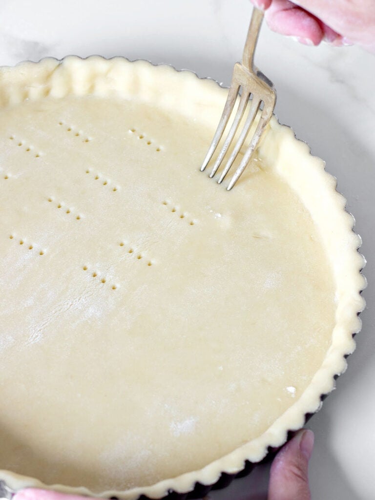 Pricking a tart crust with a fork on a white counter.