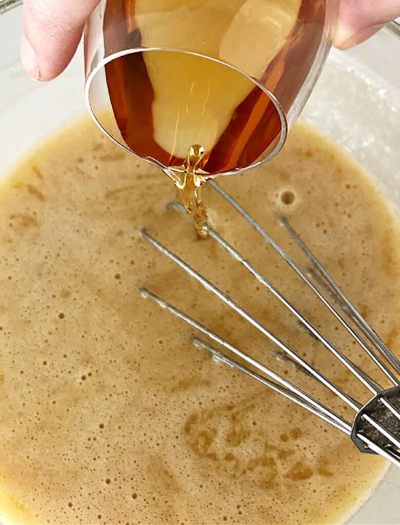 Bourbon being poured into glass bowl with brown butter and egg mixture.