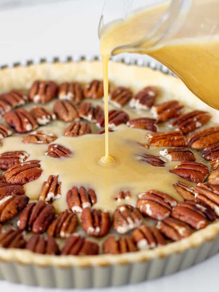 Bourbon butter filling being poured into a tart crust filled with pecans.