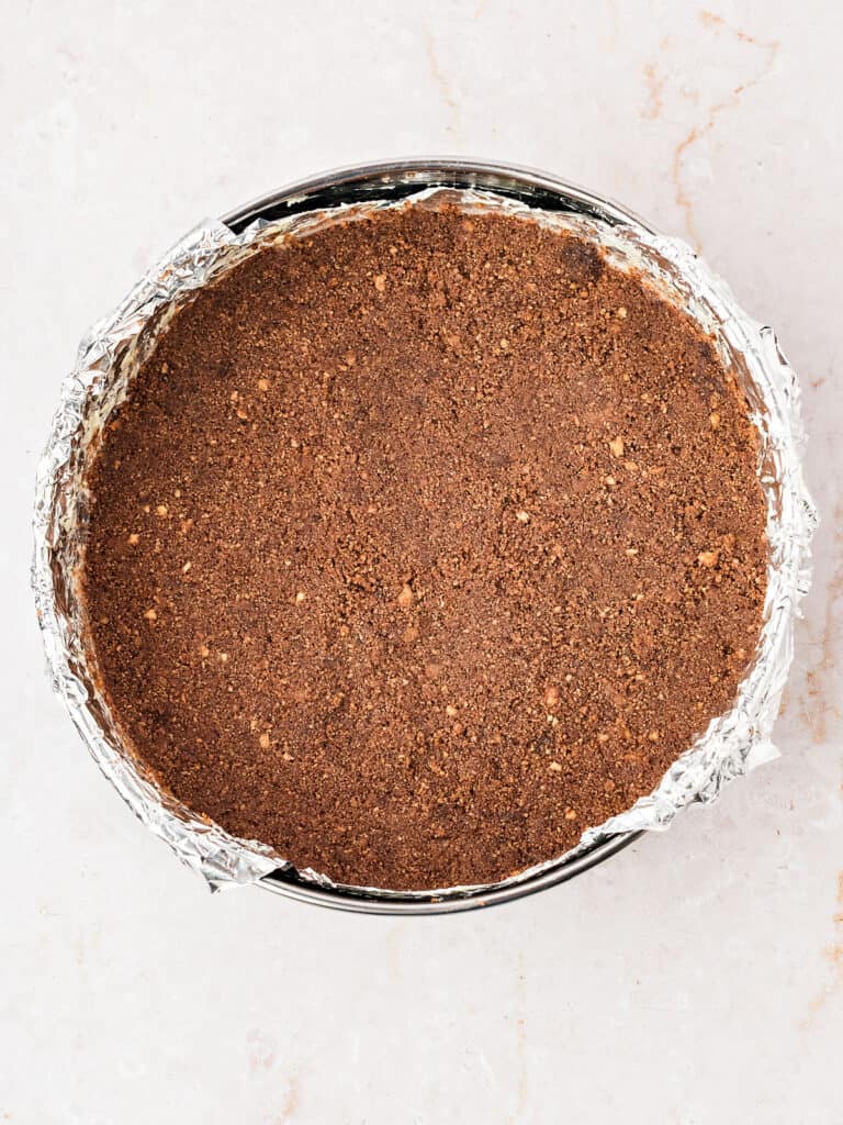 Foil-lined round cake pan with chocolate cookie crust. White background.