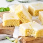 Several glazed lemon blondie squares on a wooden board. One is bitten.