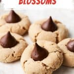 Red, white, and brown text overlay on image of several peanut butter blossom cookies on a plate.