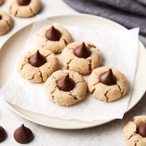 Several peanut butter chocolate blossom cookies on parchment paper on a white plate.