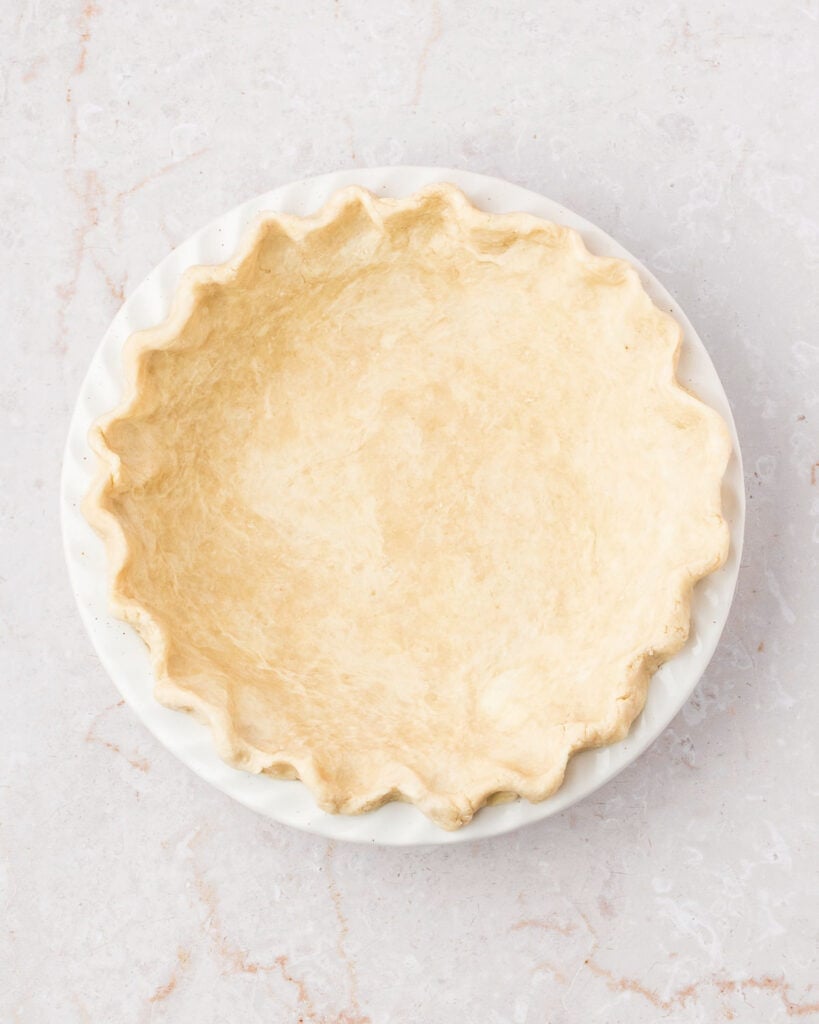 Lined white pie plate with crimped dough. White marbled background.