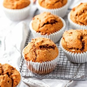 Several pumpkin muffins on a wire rack over a white kitchen cloth. White marble surface.