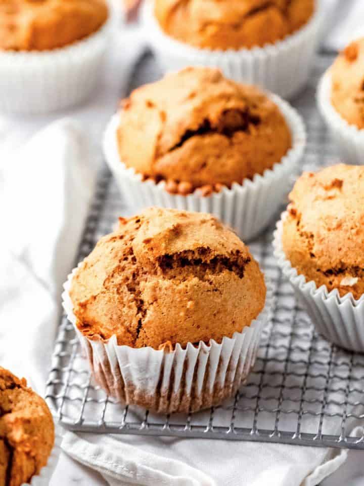 Several pumpkin muffins on a wire rack over a white kitchen cloth. White marble surface.