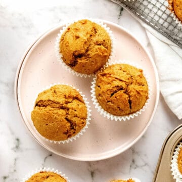 Three maple pumpkin muffins on a pink plate. White marble surface. Top view.