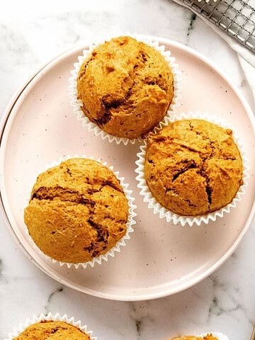 Three maple pumpkin muffins on a pink plate. White marble surface. Top view.