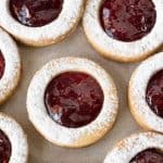 Close up of raspberry linzer cookies on a beige surface.