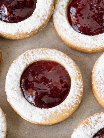 Close up of raspberry linzer cookies on a beige surface.