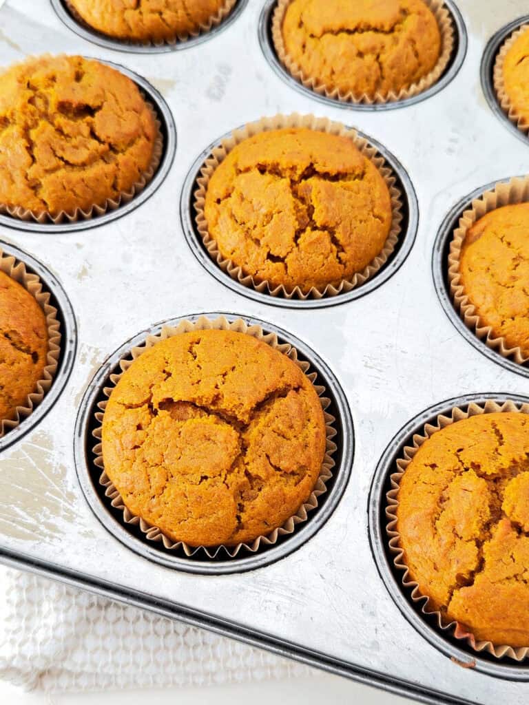 Baked pumpkin muffins in paper liners in a metal muffin tin.