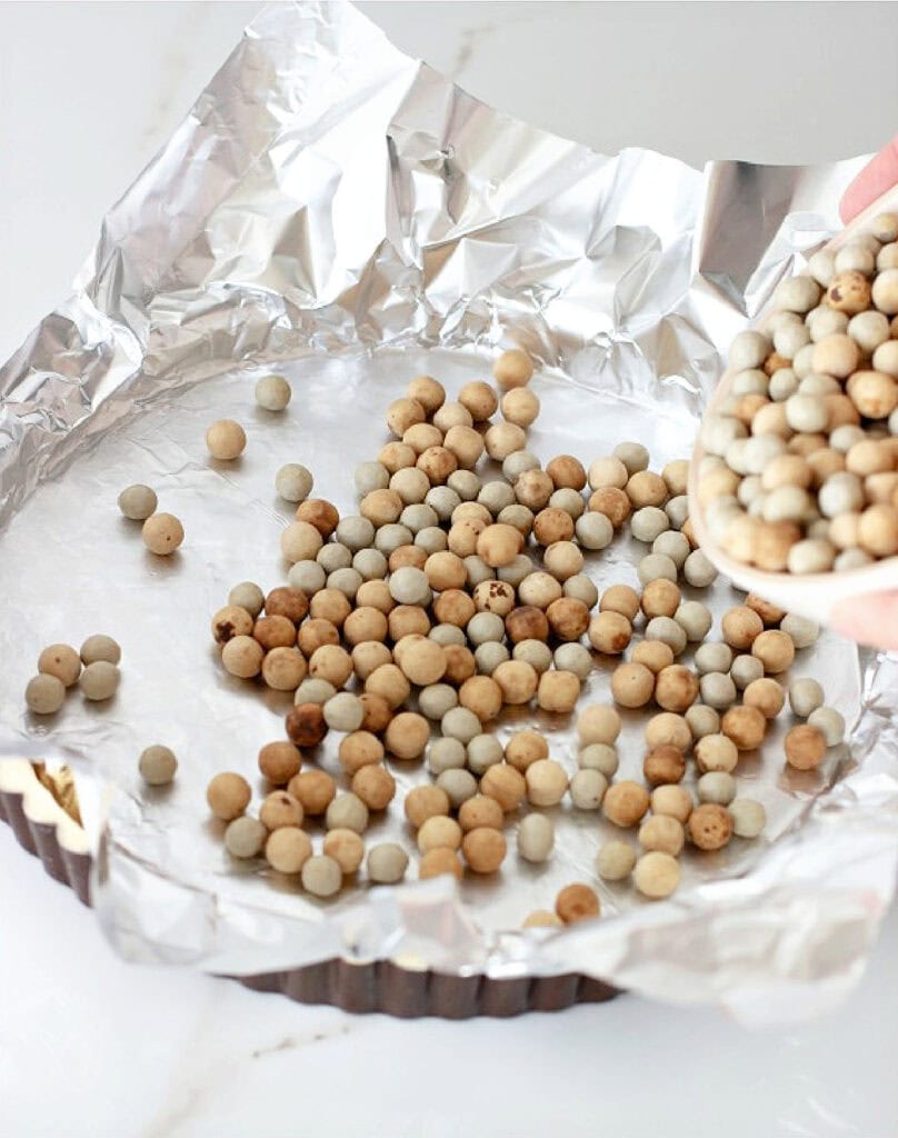 Aluminum foil with pie weights over tart crust in pan.