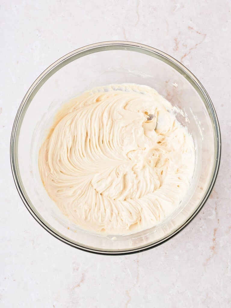 Glass bowl with cream cheese beaten with sugar. White marbled background.