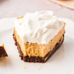 Cream-topped slice of pumpkin cheesecake with chocolate crust. White plate.