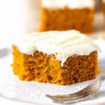 Bitten square of frosted pumpkin cake on a white plate with a silver fork.