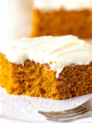 Bitten square of frosted pumpkin cake on a white plate with a silver fork.