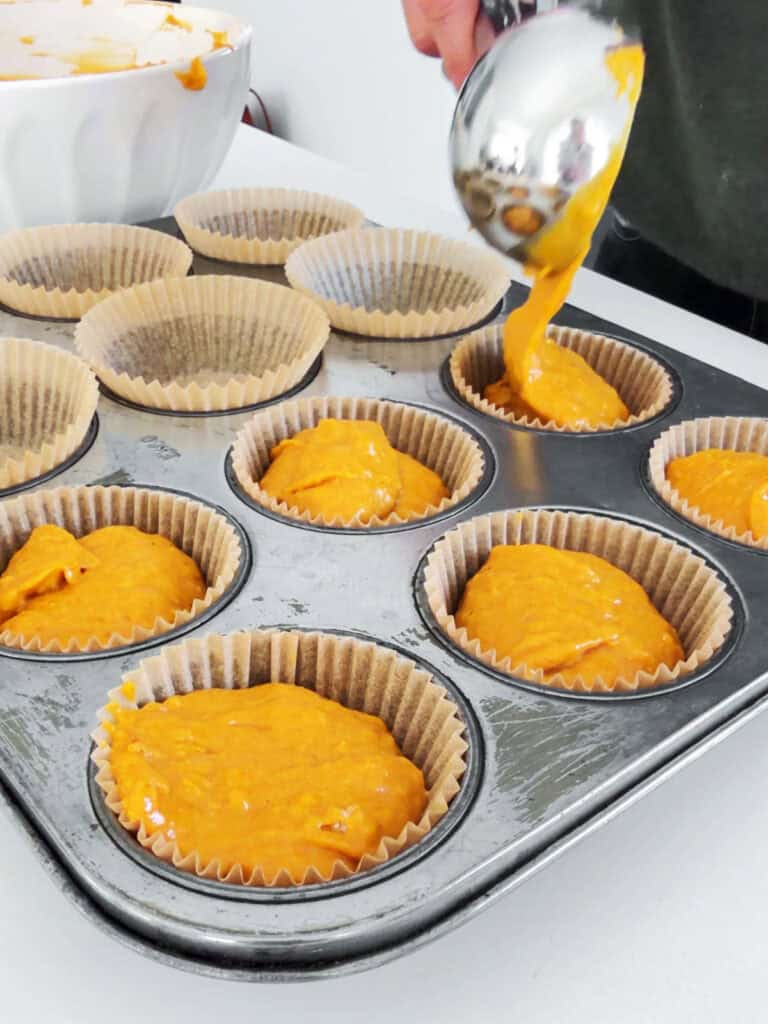 Scooping pumpkin muffin batter onto paper liners in old metal tin.