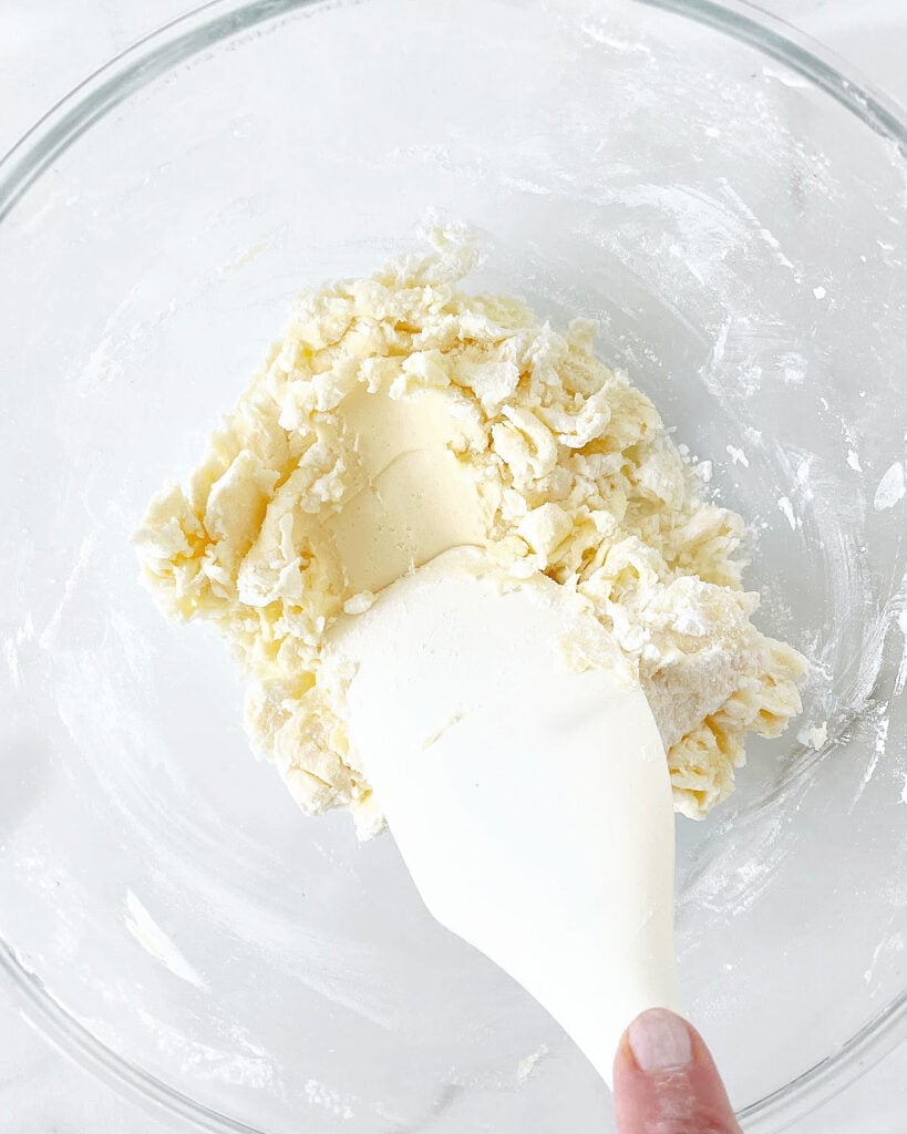 Mixing shortbread crust for tarts with a white spatula in a glass bowl.