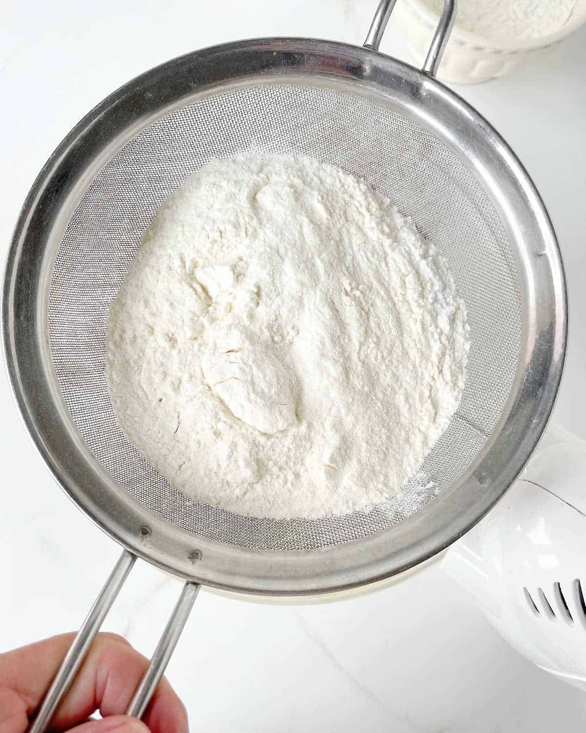 Sifting flour on top of cake batter. White surface.
