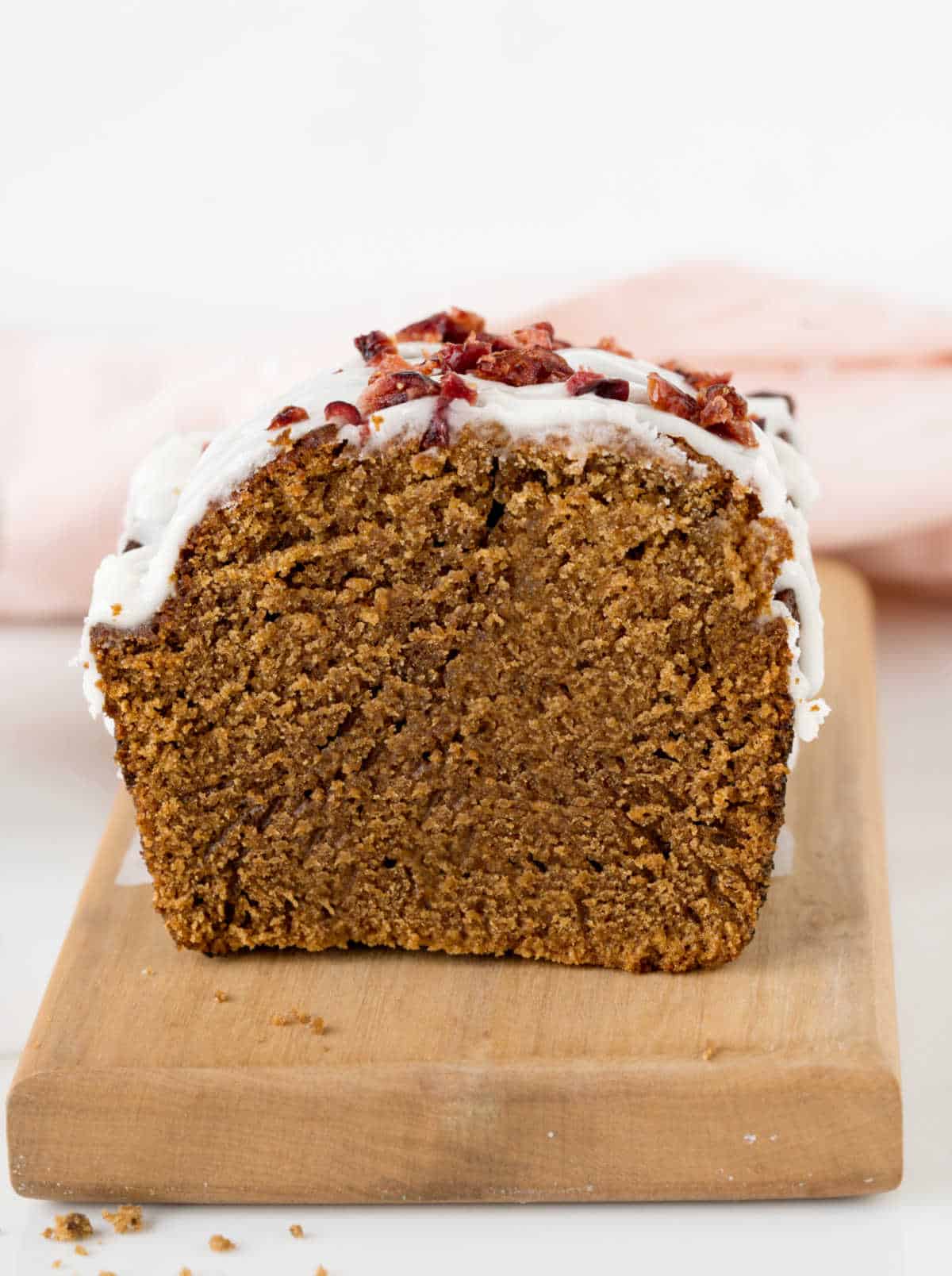 Front view of glazed gingerbread loaf on a light-colored wooden board. White and pink background.