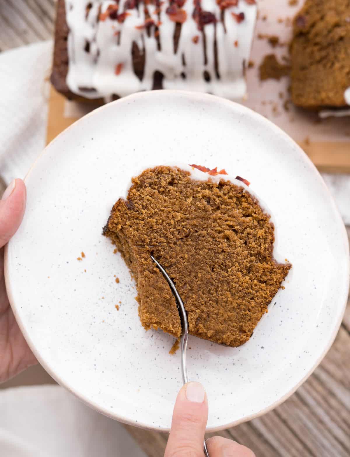 Eating a slice of gingerbread loaf on a white plate with a silver fork. View from above. 