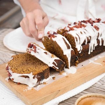 Glazed gingerbread loaf cake on a wooden board being sliced.