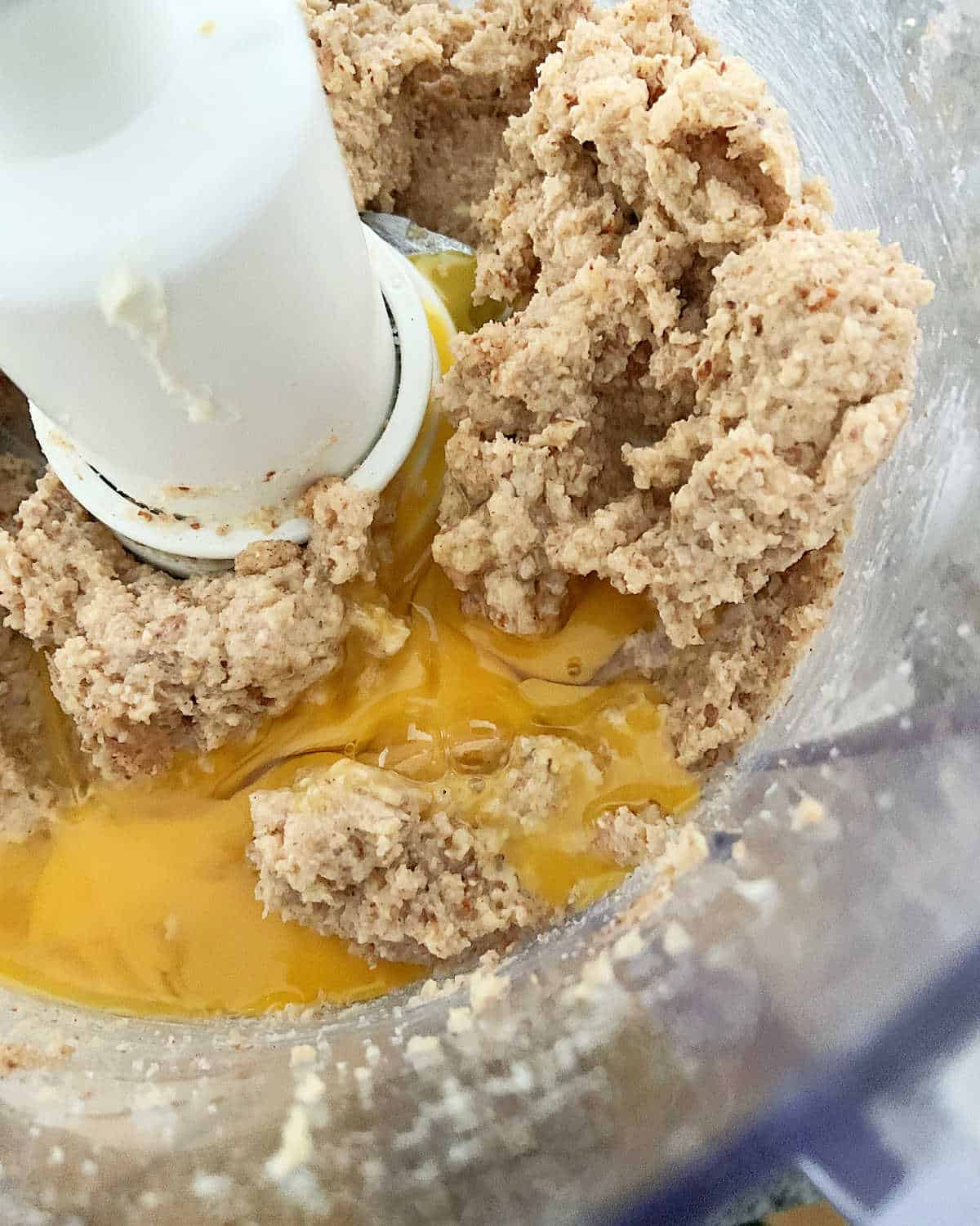 Egg added to the bowl of a food processor with almond butter mixture.