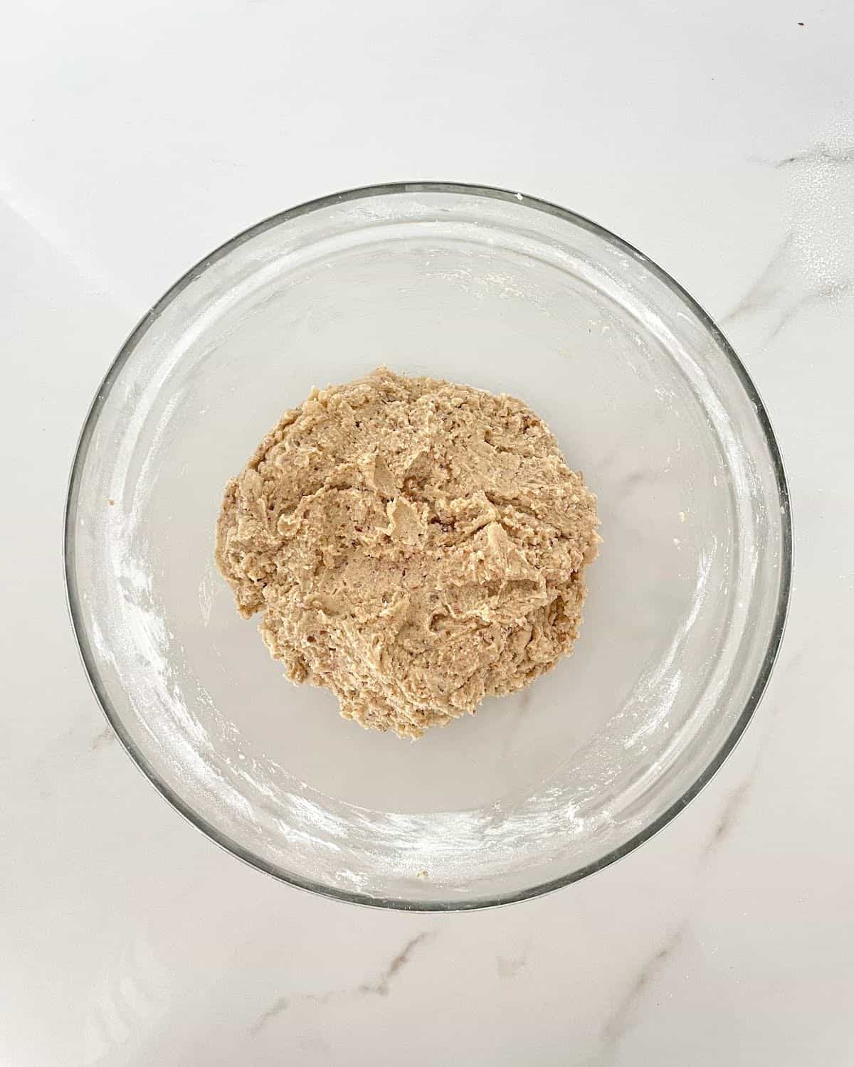 Pecan cookie dough in a glass bowl on a white marble surface.