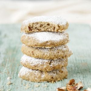 Stack of pecan cookies on a green wooden surface. Top one is bitten.