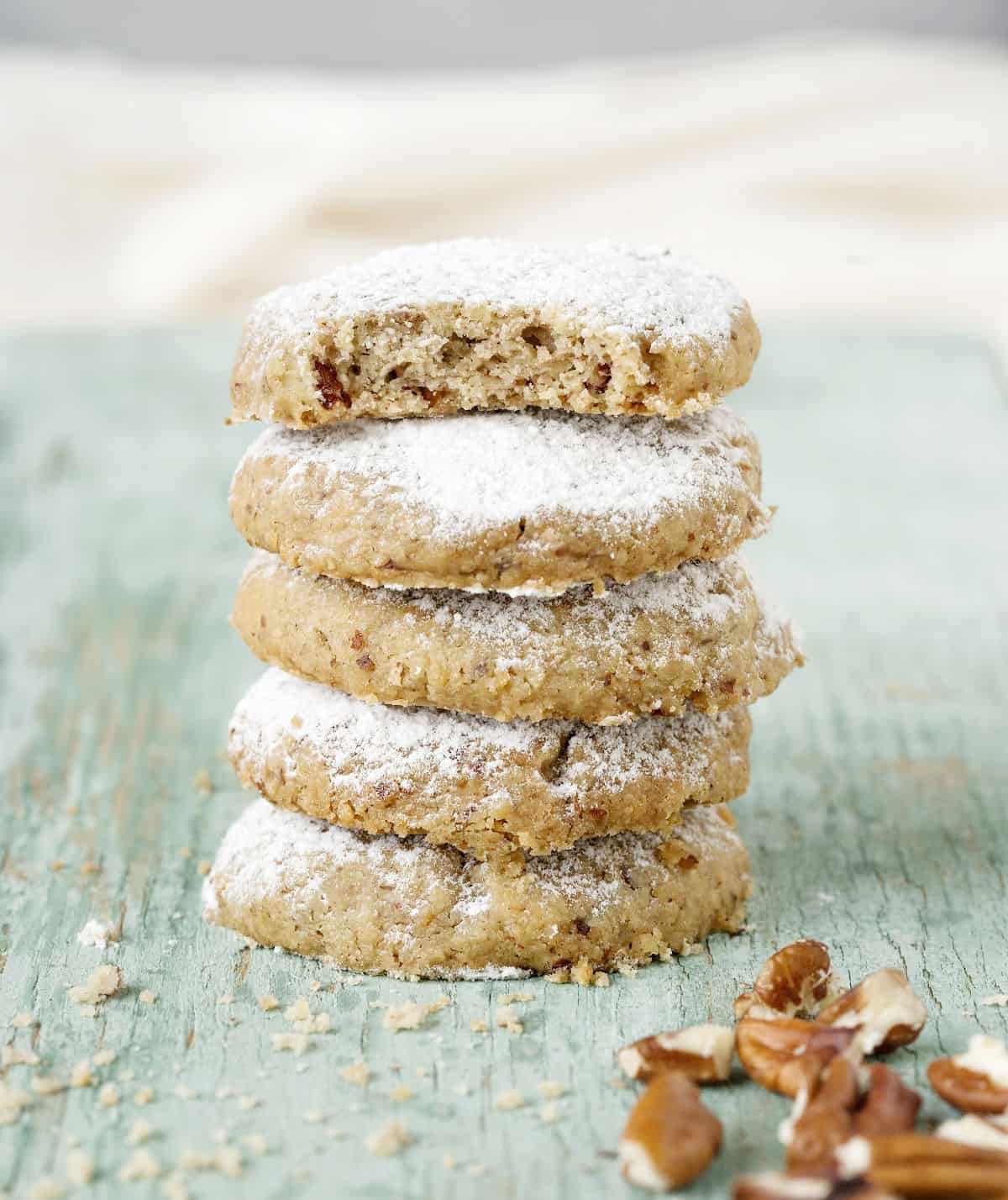 Several pecan sandies in a stack with top one bitten. Green wooden surface. 