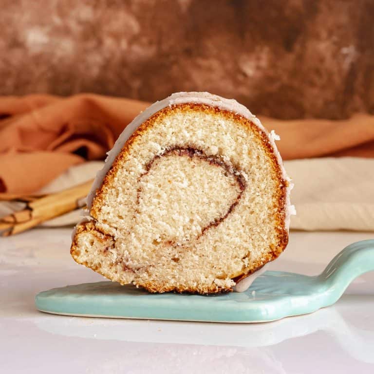 Blue cake server with slice of cinnamon swirl bundt cake. Brown background.
