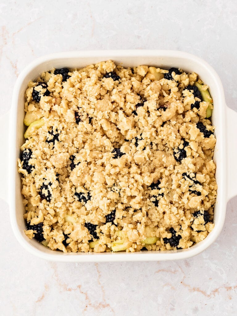 Crumble topped apple blackberry crumble before baking. White dish.