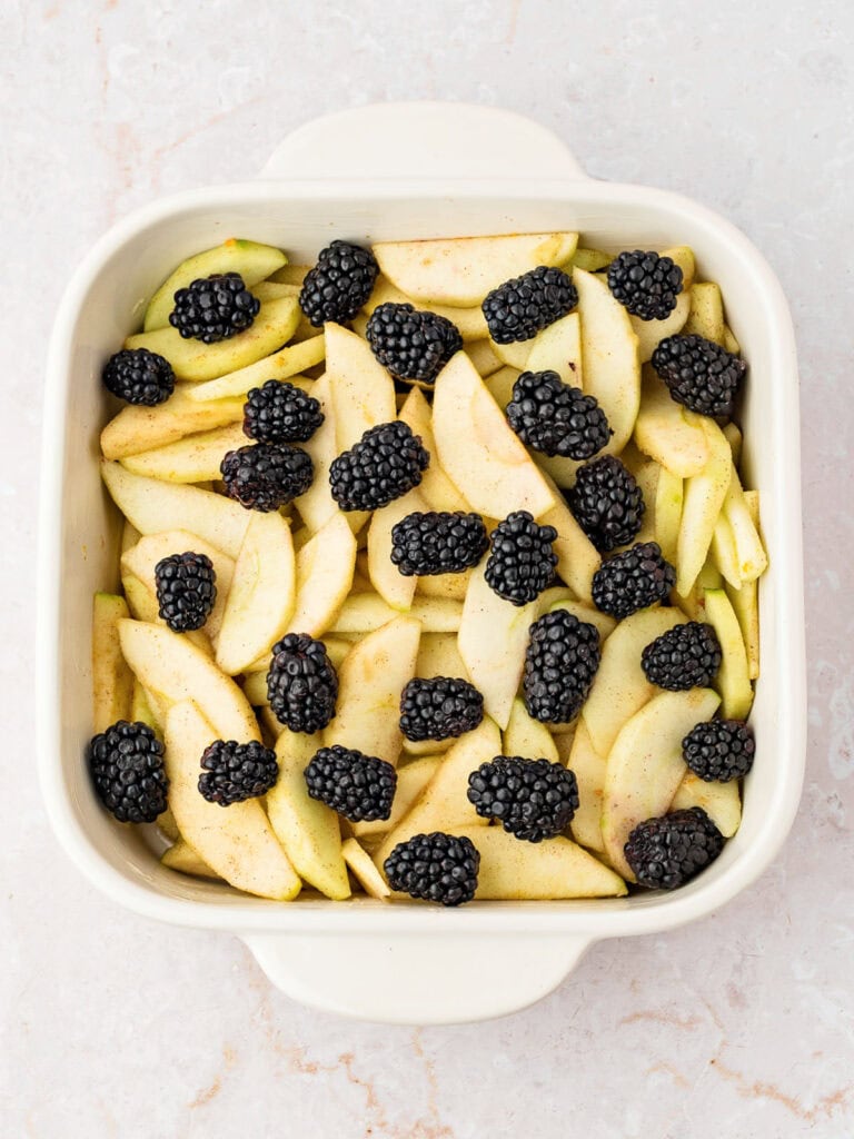 White dish with apple slices and blackberries. White background.