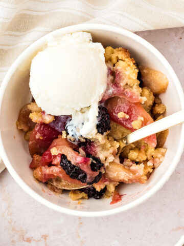 White bowl of apple blackberry crumble with ice cream. Beige background.