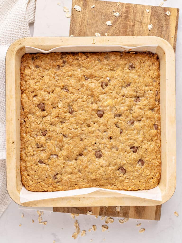Beige pan on a wooden board with baked oat chip bars.
