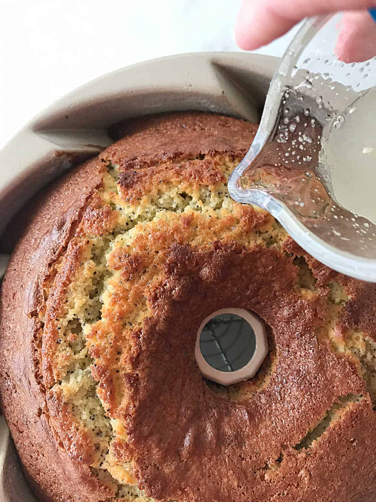 Pouring syrup over baked lemon poppy bundt cake in the pan.