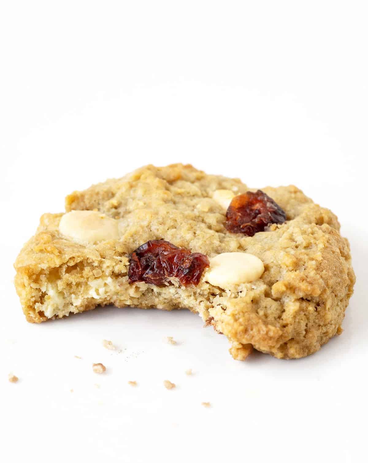 Bitten cranberry white chocolate chip oatmeal cookie on a white surface.