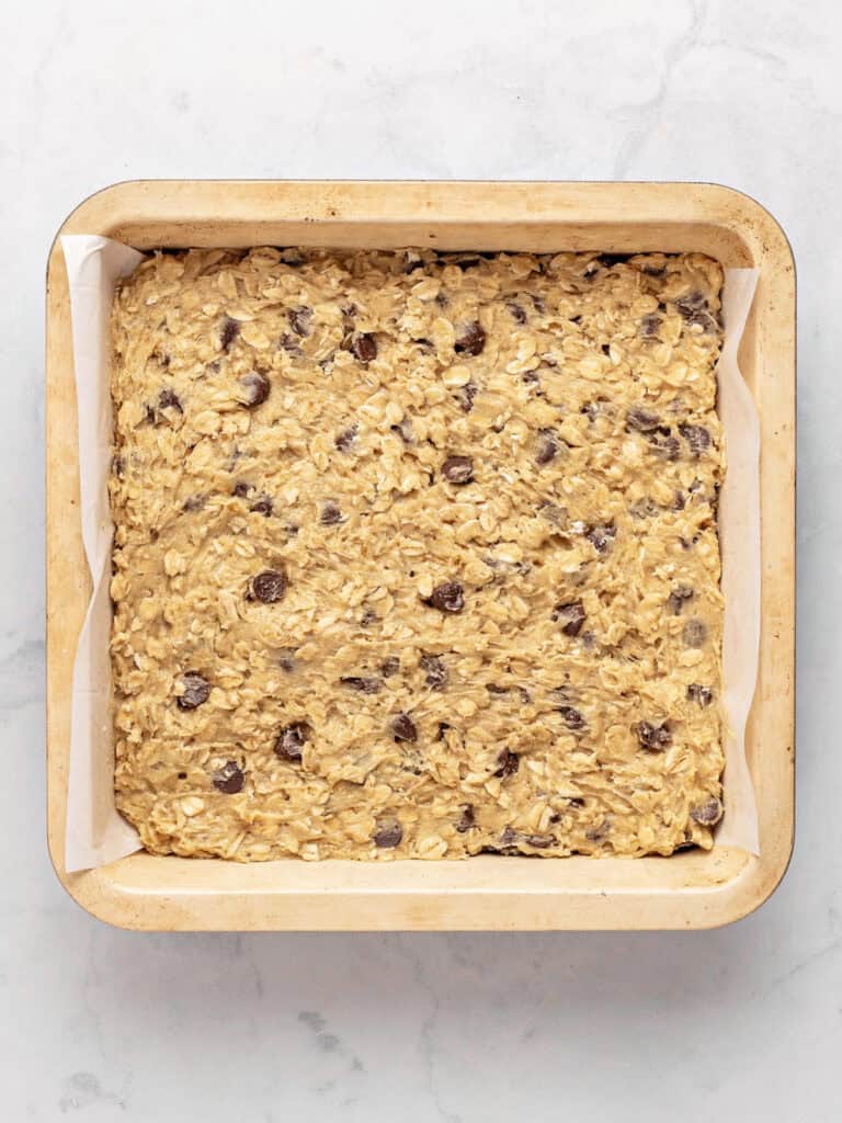 Parchment-lined beige pan with chocolate chip oat bars before baking.