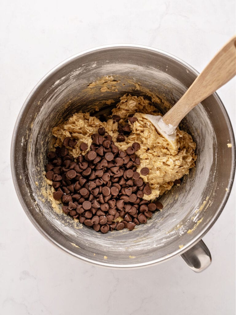 Metal bowl with oatmeal bars batter and chocolate chips. Wooden spoon.