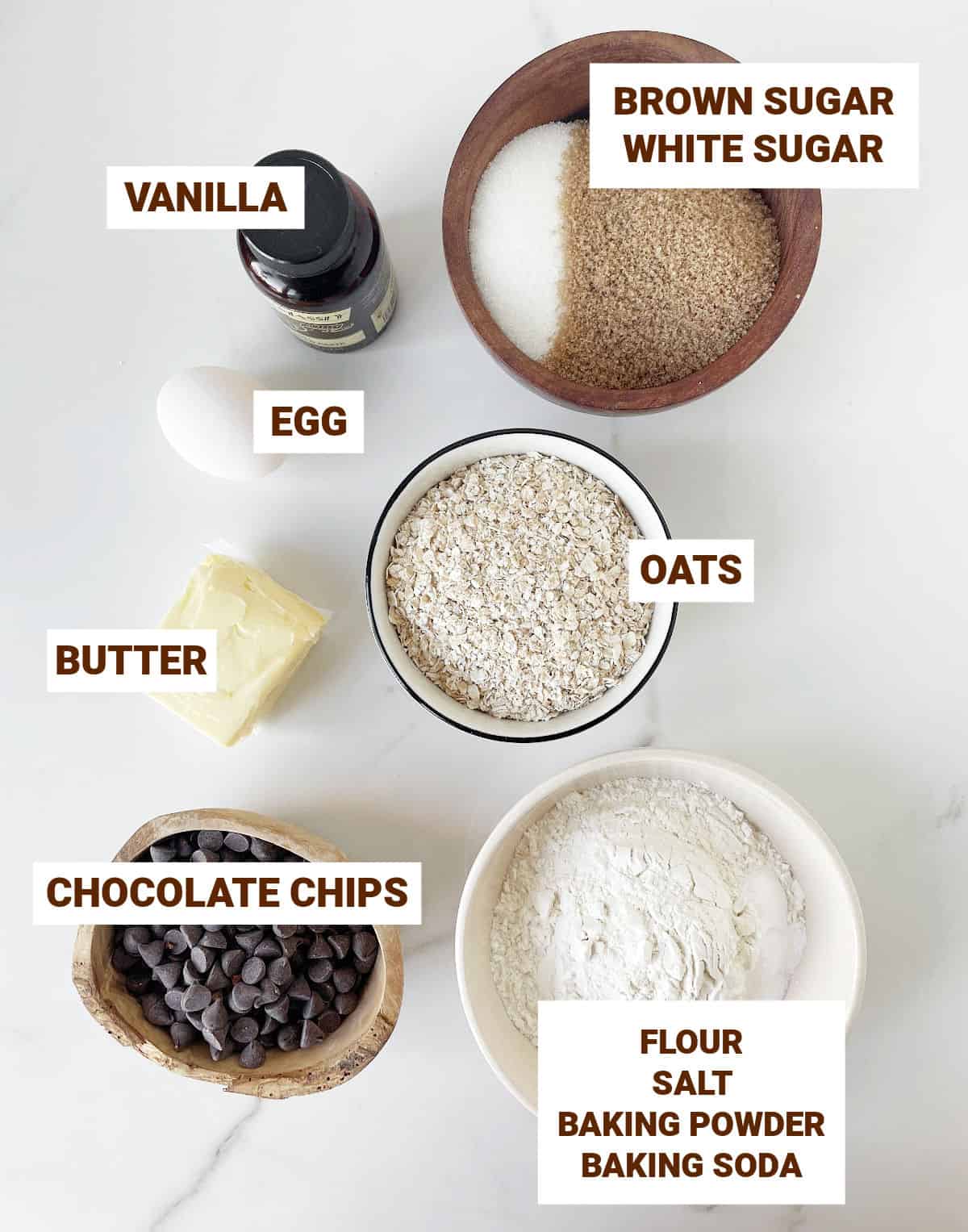 White marble with bowls containing ingredients for chocolate chip oatmeal bars including butter, sugars, vanilla, egg, flour mixture.