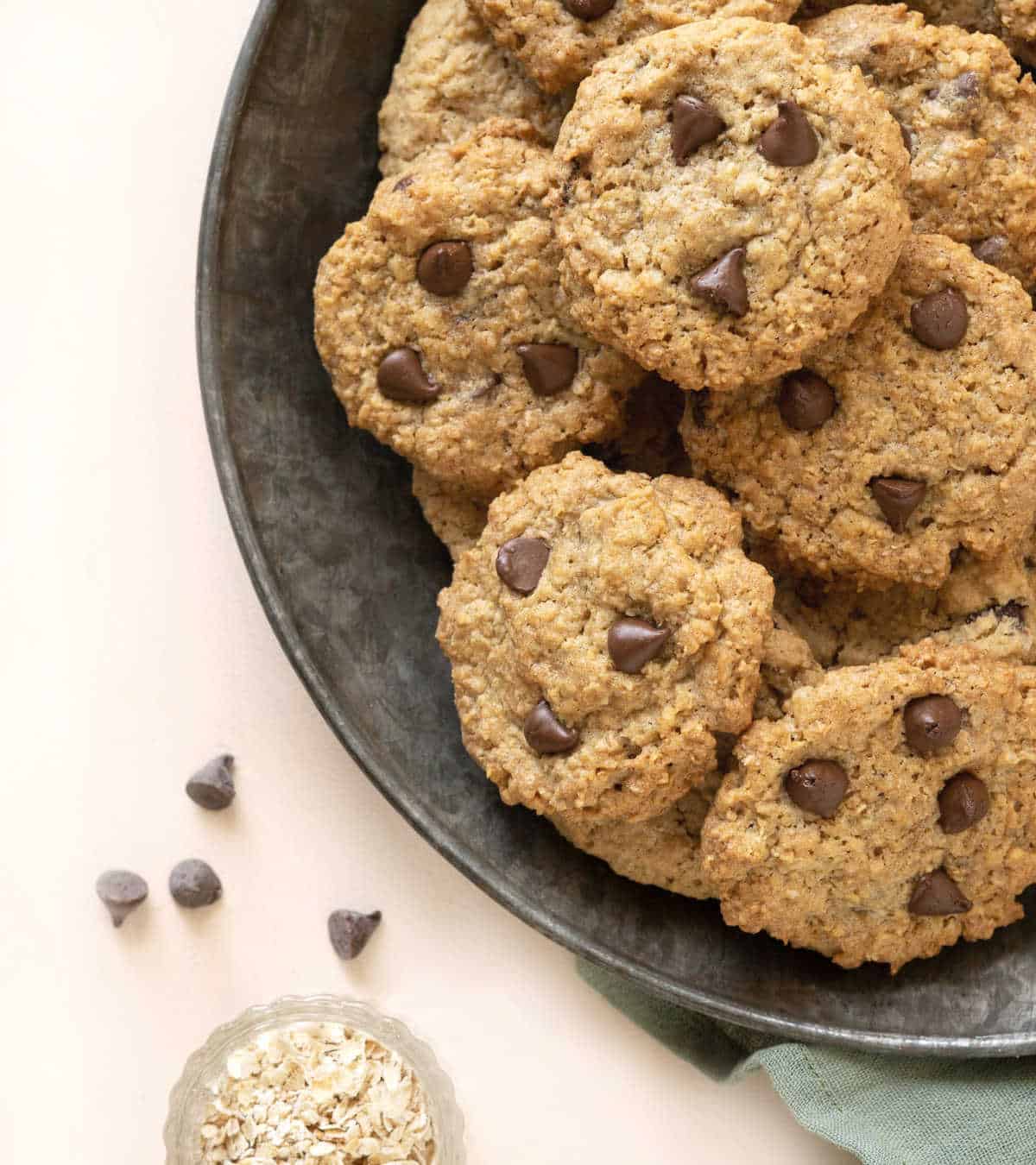 A metal plate with chocolate chip oatmeal cookies in a pile. Light peach surface. 