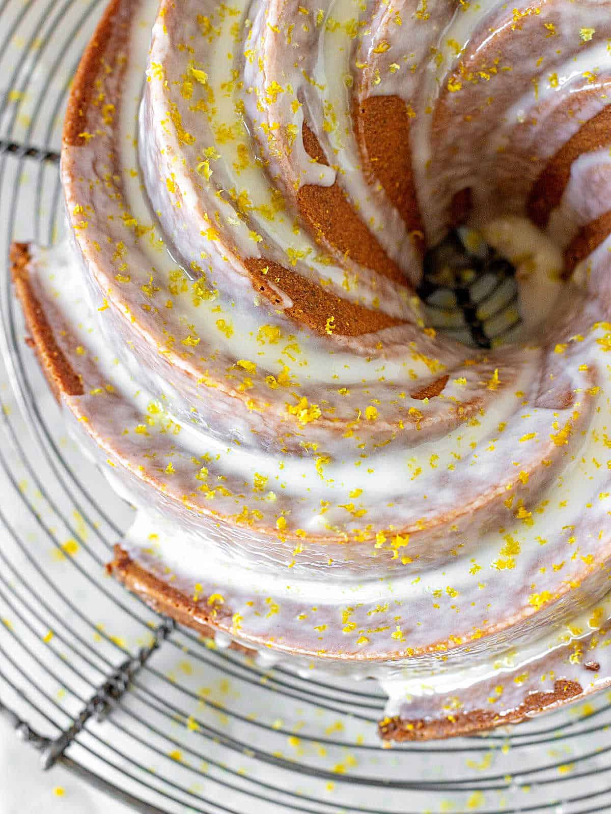 Top view of partial glazed bundt cake with lemon zest on a wire rack.