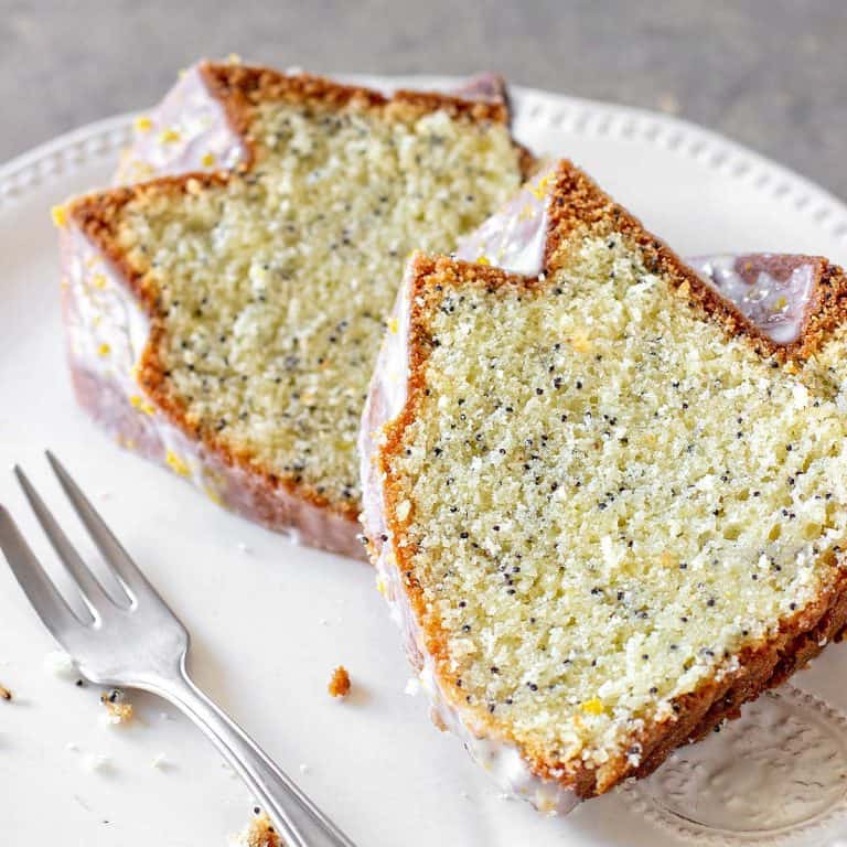 White plate with two slices of lemon poppy seed cake, a silver fork, grey background.