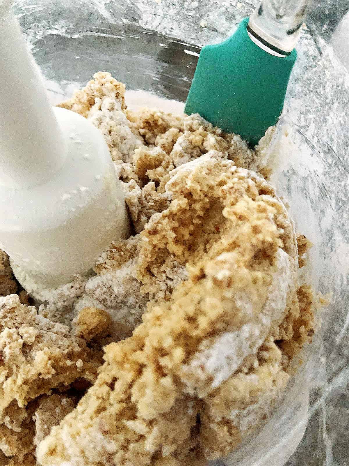 Scraping spiced dough mixture with a spatula in a food processor.