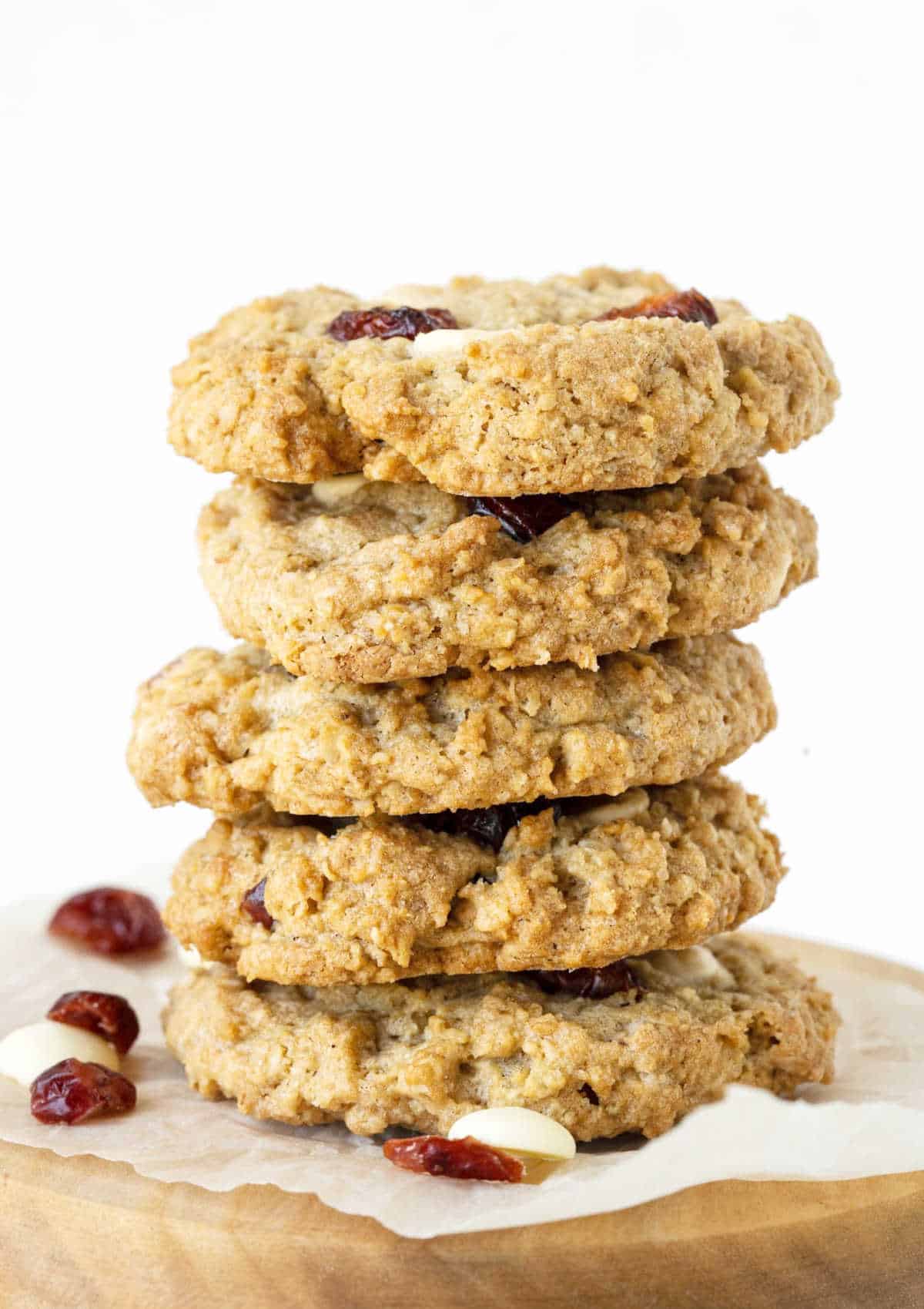 Stack of white chocolate cranberry oatmeal cookies on parchment paper on a wooden board. White background. 