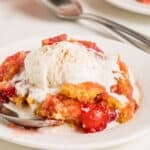 Close up white plate with pineapple cherry dump cake with ice cream. Silver spoons, white background.