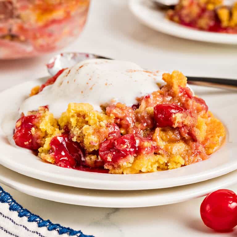 Stacked white plates with pineapple cherry dump cake serving with ice cream. White background.