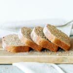 Several leaning whole wheat bread slices on a wooden board. White background.